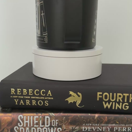 Black stainless steel mug with 'in my bookish era' and books engraved around it, set on top of a stack of black and gold books.