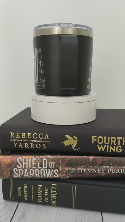 Black stainless steel mug with 'in my bookish era' and books engraved around it, set on top of a stack of black and gold books.
