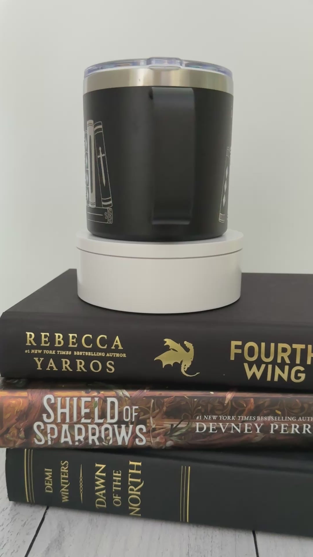 Black stainless steel mug with 'in my bookish era' and books engraved around it, set on top of a stack of black and gold books.