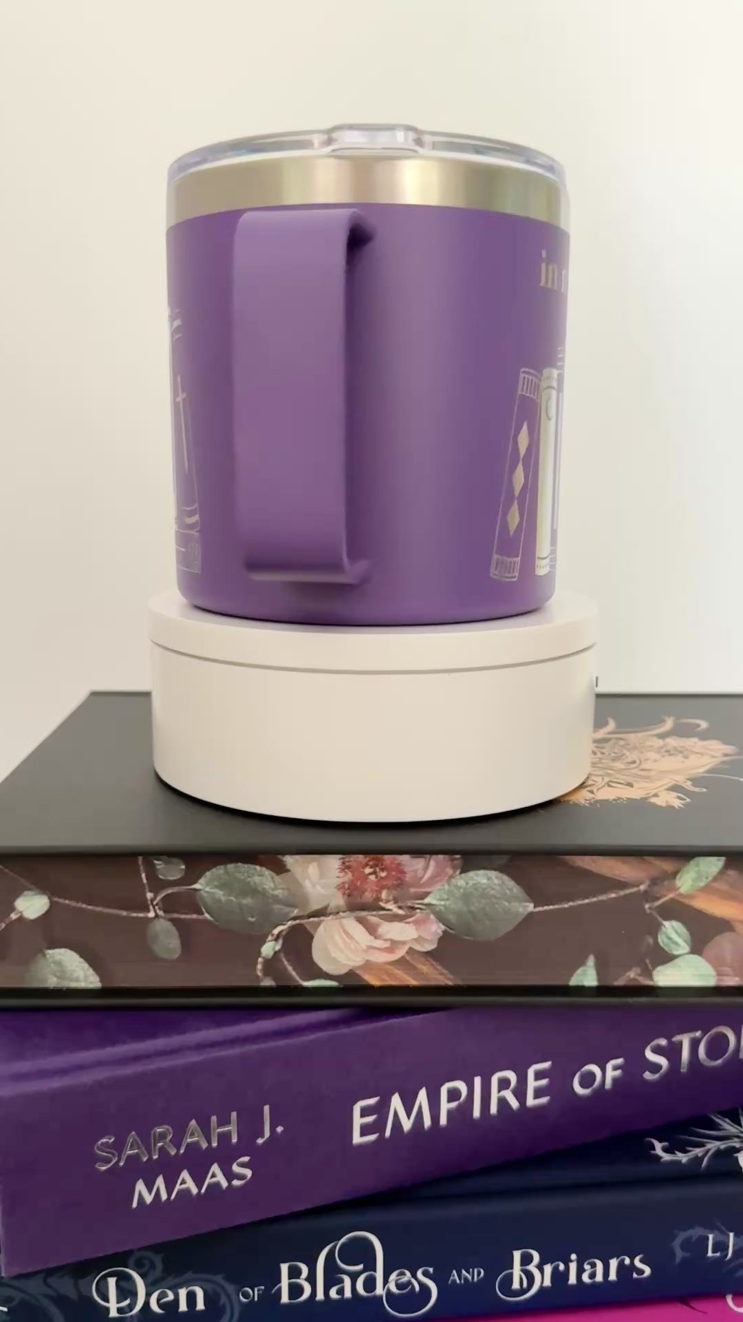 Purple stainless steel mug with 'in my bookish era' and books engraved around it, set on top of a stack of purple and black books.