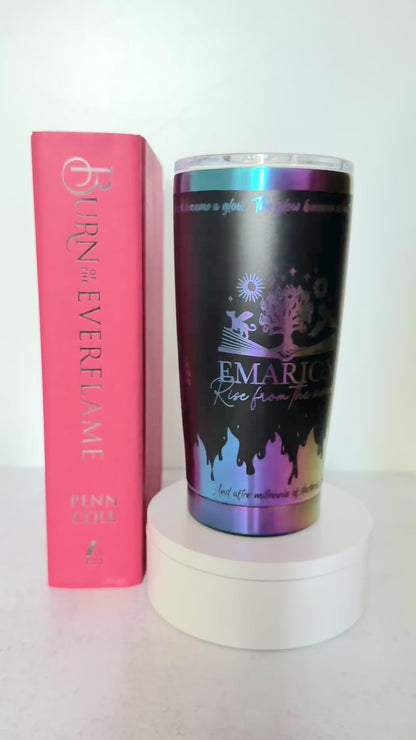Slow turn of a black and rainbow iridescent 20 oz Emarion tumbler with Everflame tree, phoenix and gryvern exploding from an open book and other world elements from  the Kindred's Curse Saga, next to a copy of Burn of the Everflame