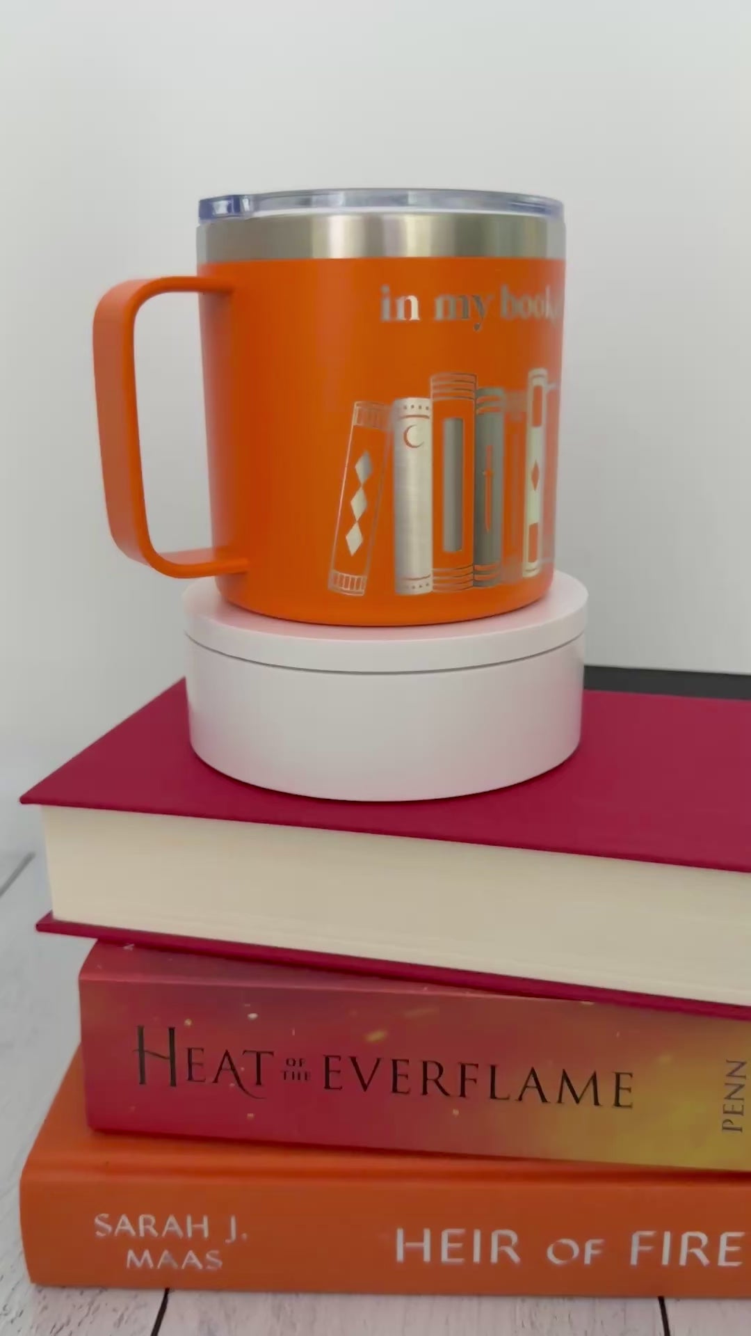 Orange stainless steel mug with 'in my bookish era' and books engraved around it, set on top of a stack of orange and red books.