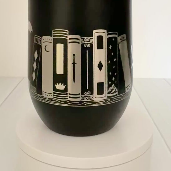 black wine tumbler spinning around, engraved with "in my bookish era" and books on a book shelf