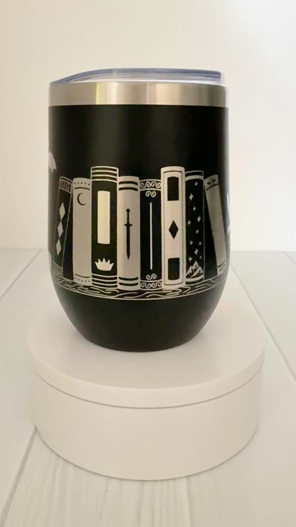 black wine tumbler spinning around, engraved with "in my bookish era" and books on a book shelf