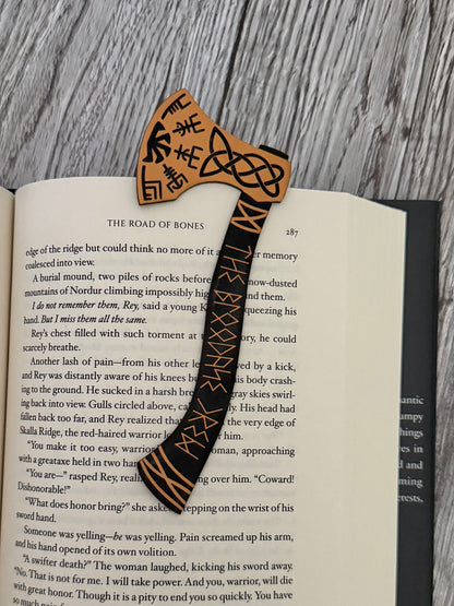 Acrylic engraved bookmark shaped like a viking axe with celtic knots and runes on an open book of The Road of Bones by Demi Winters.