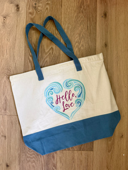 Tote bag with blue waves in a heart design and 'Hello Love' text, inspired by The Ever King by LJ Andrews, on a wooden surface