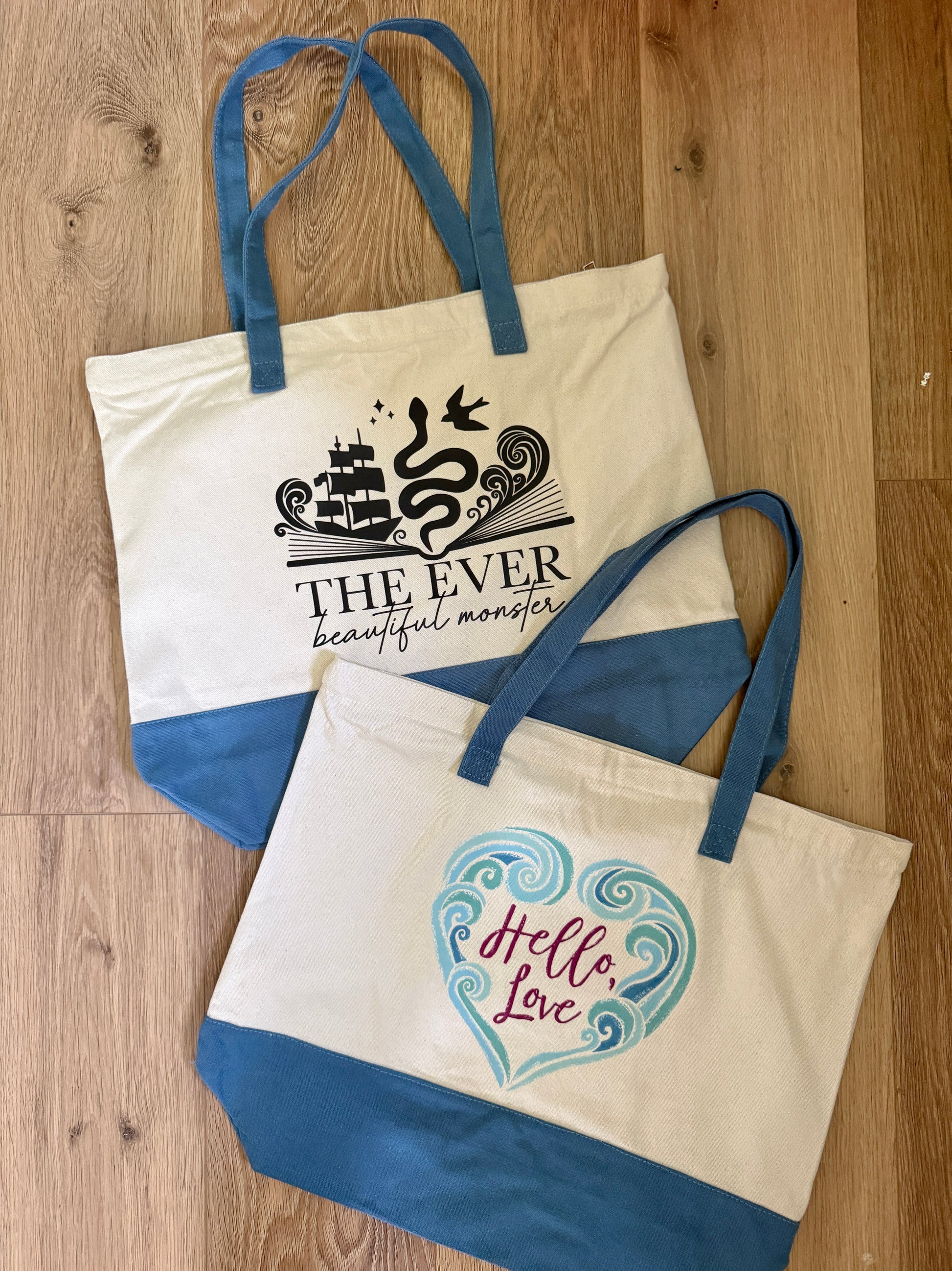 Two tote bags with printed designs including 'Hello Love' inspired by the Ever King by LJ Andrews on a wooden surface