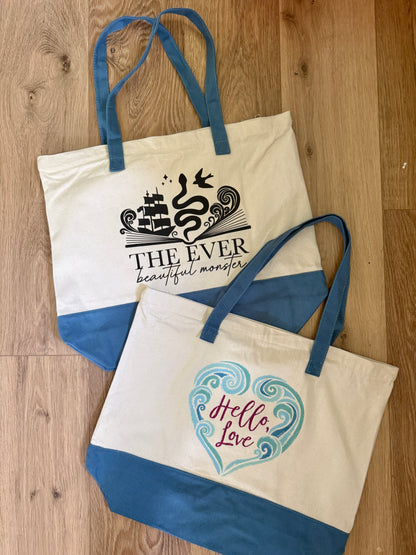 Two tote bags with printed designs including 'Hello Love' inspired by the Ever King by LJ Andrews on a wooden surface