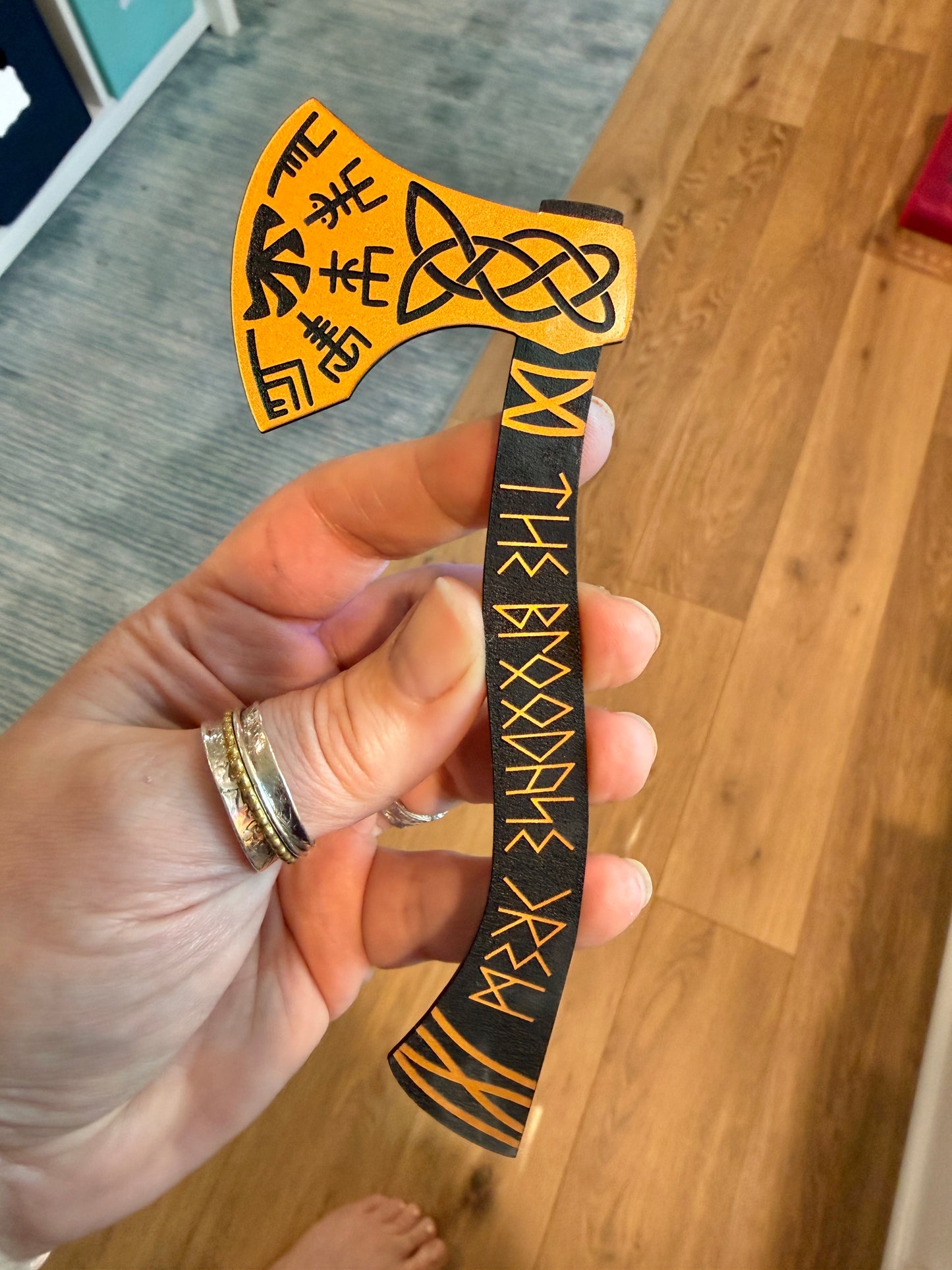 Hand holding a decorative axe bookmark with Viking design and The Bloodaxe Crew in runes on a wooden floor.